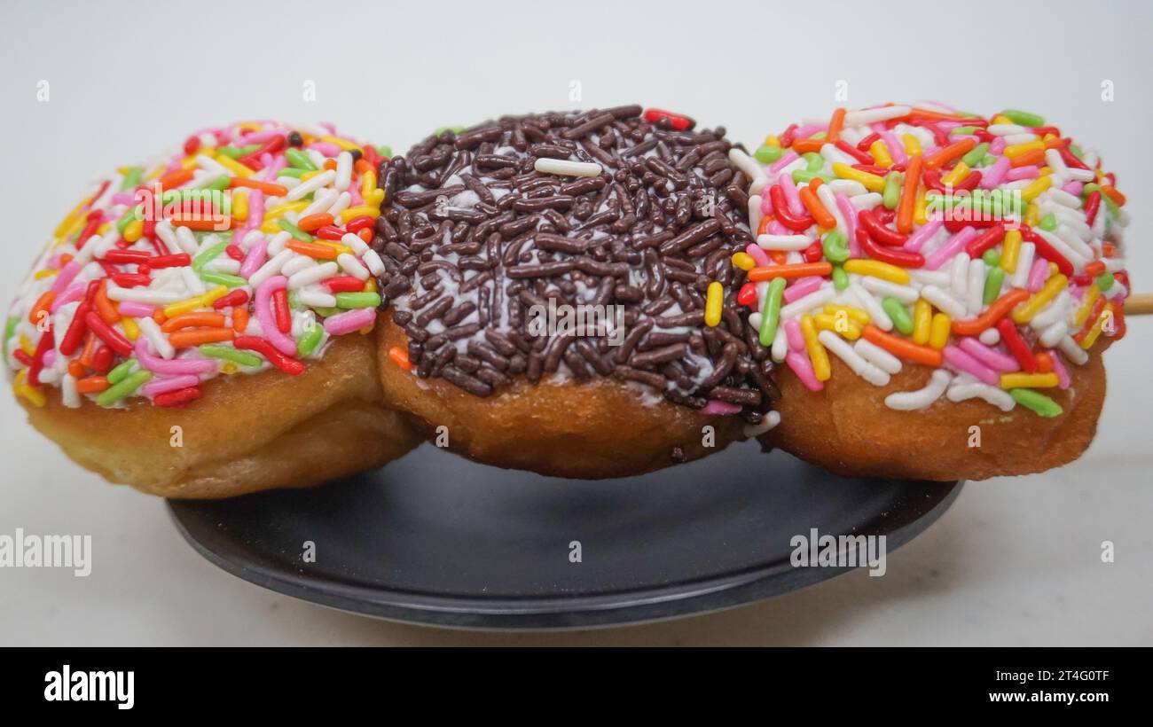 Donuts mit bunten Streuseln und Schokoladenstreusel auf Spießen wie Satay auf einem schwarzen Teller Stockfoto
