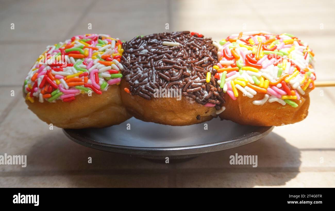 Donuts mit bunten Streuseln und Schokoladenstreusel auf Spießen wie Satay auf einem schwarzen Teller Stockfoto