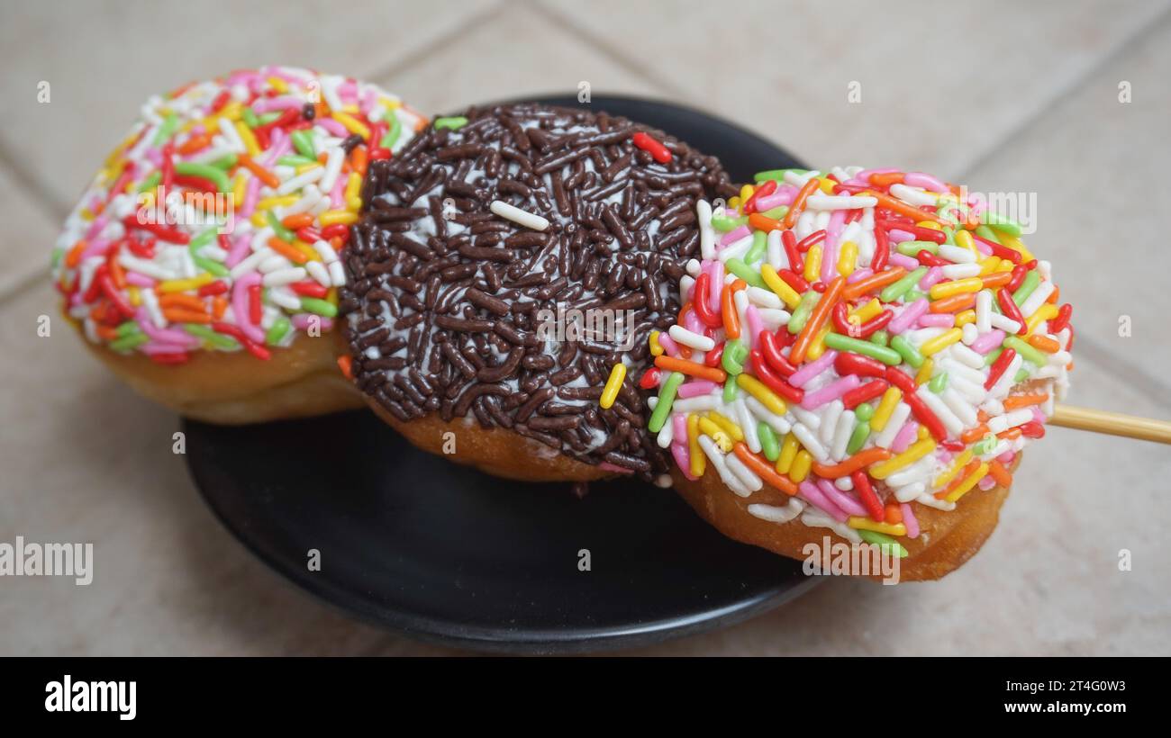 Donuts mit bunten Streuseln und Schokoladenstreusel auf Spießen wie Satay auf einem schwarzen Teller Stockfoto