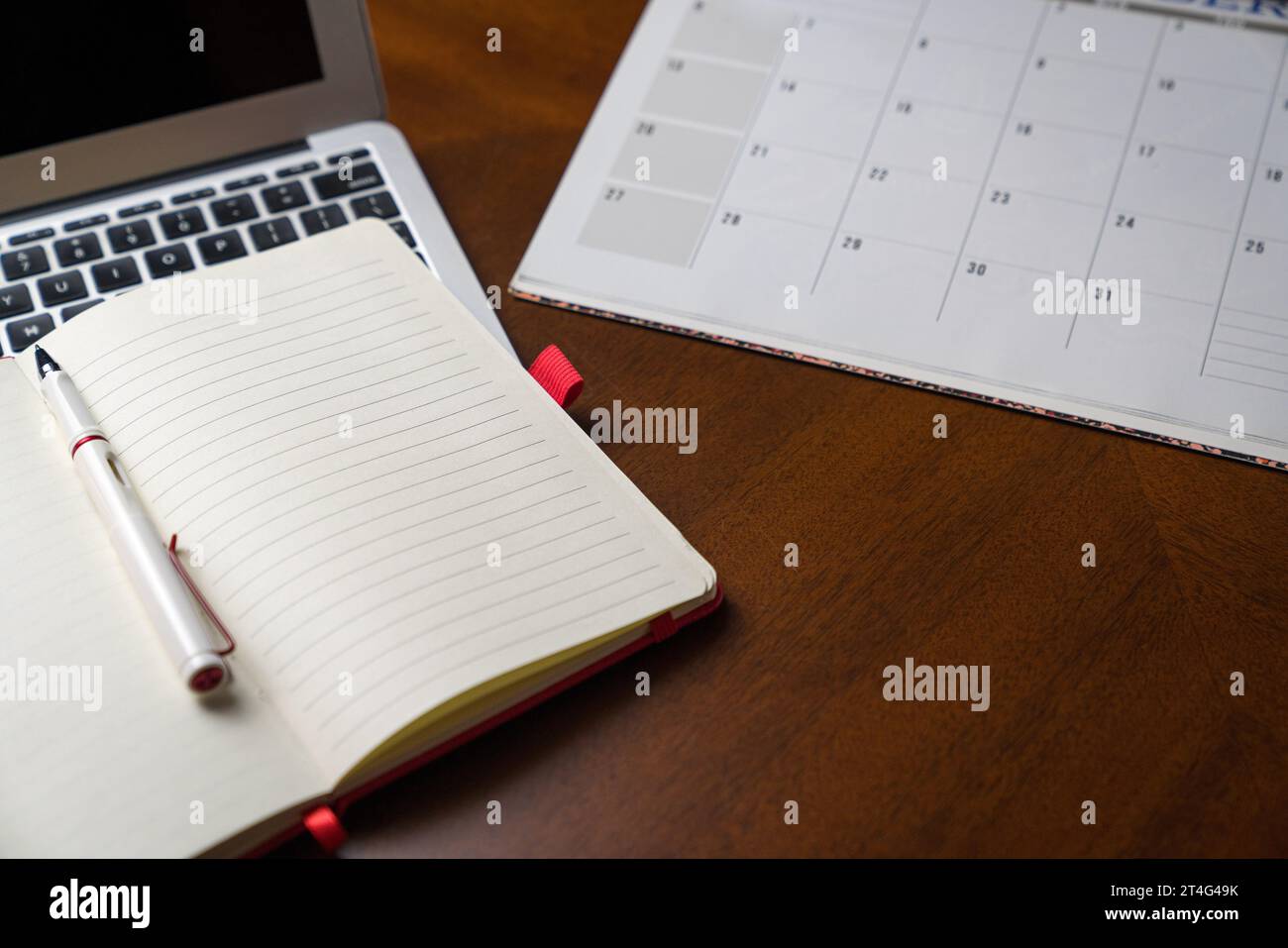 Notizblock auf dem Laptop und neben Kalender oder Planer. Auf dem Holztisch. Kopierbereich. Stockfoto