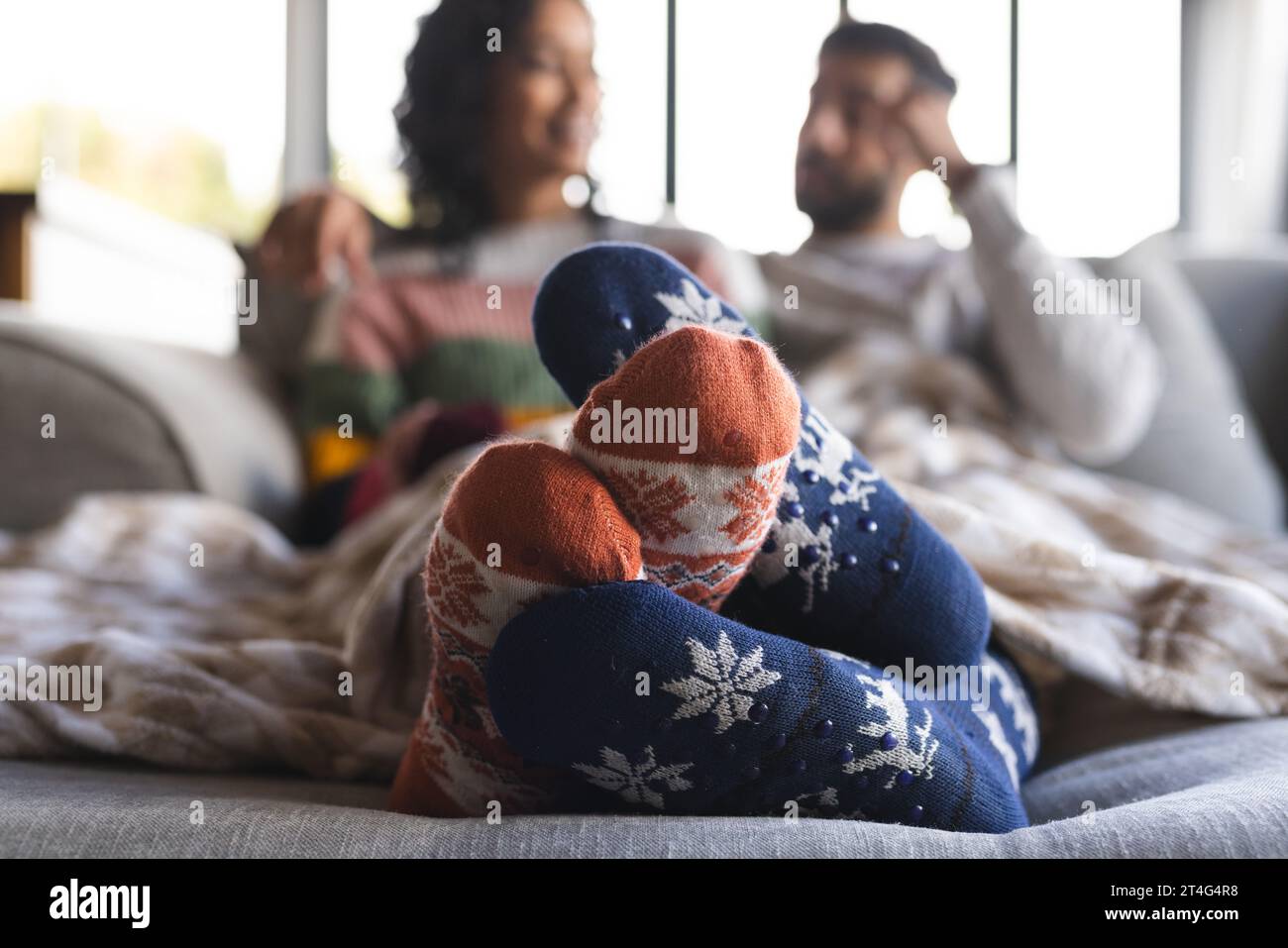 Glückliches birassisches Paar in warmen Socken, das sich auf dem Sofa im Wohnzimmer zu Hause umschließt Stockfoto