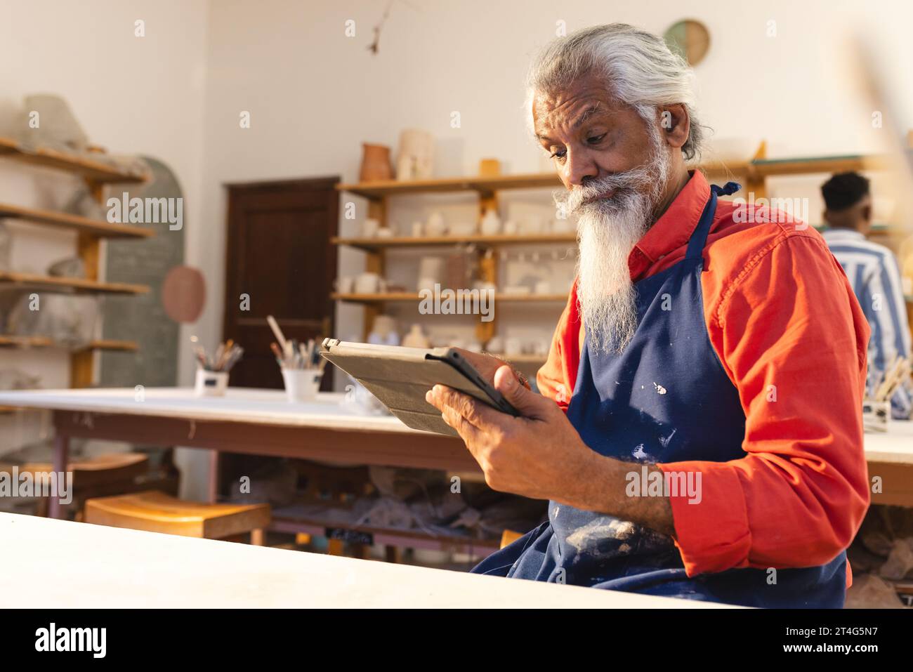 Fokussierter birassischer älterer Töpfer mit langem Bart mit Tablette im Töpferstudio Stockfoto