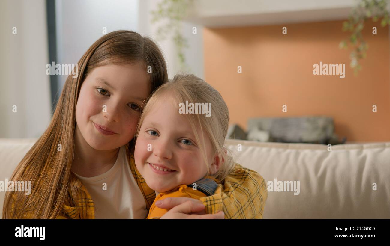 Porträt glücklich süß kleine kaukasische Mädchen Kinder Schwestern Kinder Freunde lächelnd Blick sich gegenseitig umarmen umarmen Kuschel aussehende Kamerafamilie Stockfoto