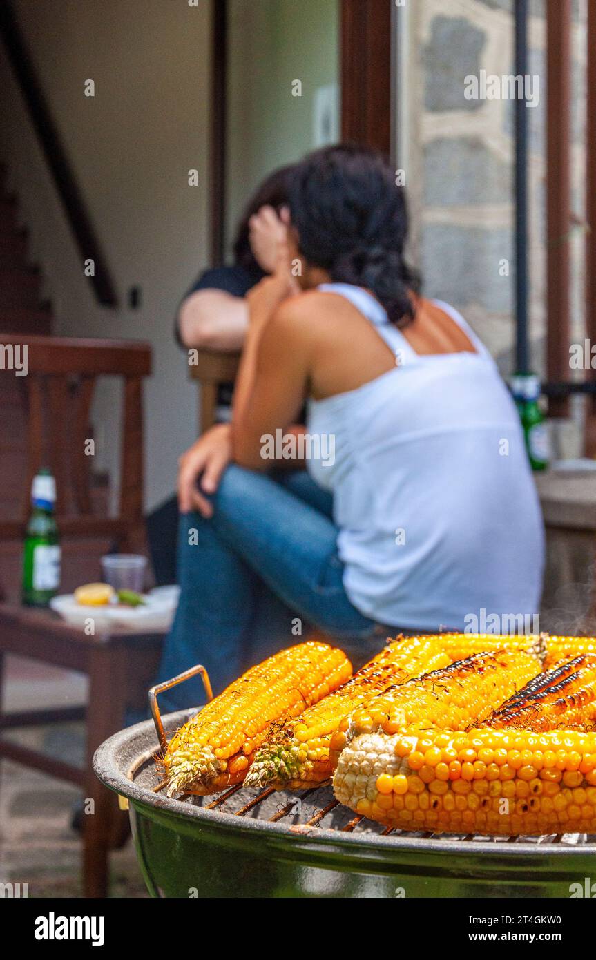 Nahaufnahme von gegrilltem Mais im Garten mit Mädchenrücken im Hintergrund Stockfoto