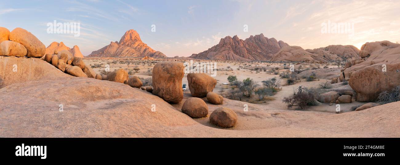 Panoramablick, Wüstenlandschaft mit berühmten runden roten Granitfelsen der Spitzkoppe Gegend bei frühem Sonnenaufgang vor blauem Himmel. Malerisches Foto der felsigen Wüste Stockfoto