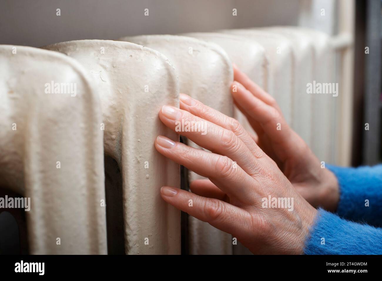 Eine weiße Frau hält ihre Hände am Heißwasserstrahler. Heizungskonzept. Leerzeichen für Text Stockfoto