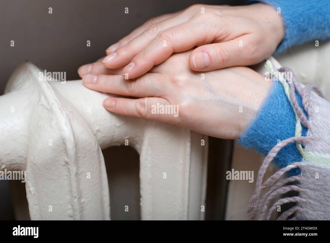 Eine weiße Frau hält ihre Hände am Heißwasserstrahler. Heizungskonzept. Leerzeichen für Text Stockfoto