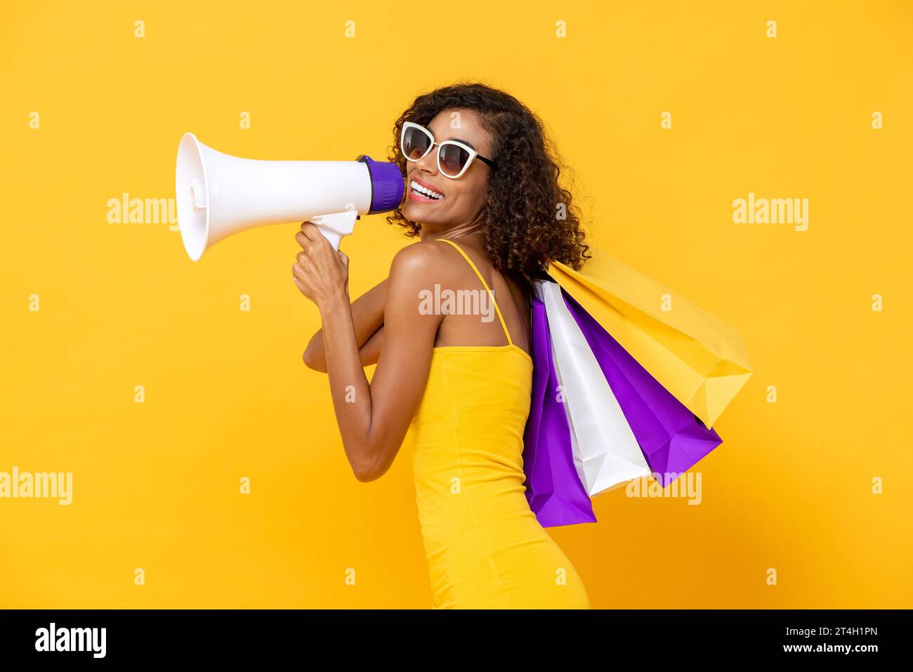 Schöne Frau, die Einkaufstaschen trägt und auf Megaphon im isolierten gelben Farb-Studiohintergrund für Sommerverkauf spricht Stockfoto