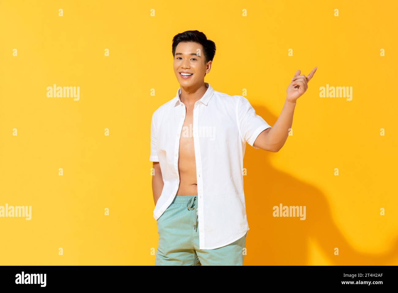Sommerporträt eines lächelnden gutaussehenden asiatischen Mannes, der den Finger nach oben zeigt, in gelbem Farb-Studio-Hintergrund Stockfoto Sommerporträt eines lächelnden gutaussehenden asiatischen Mannes, der den Finger nach oben zeigt, in gelbem Farb-Studio-Hintergrund Stockfoto