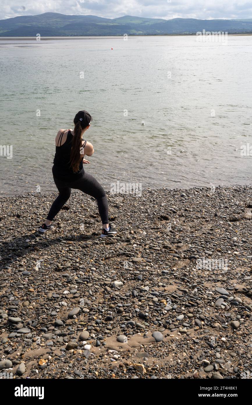 Ein junges Weibchen, das Steine im Meer in Aberaeron Beach überspringt Stockfoto
