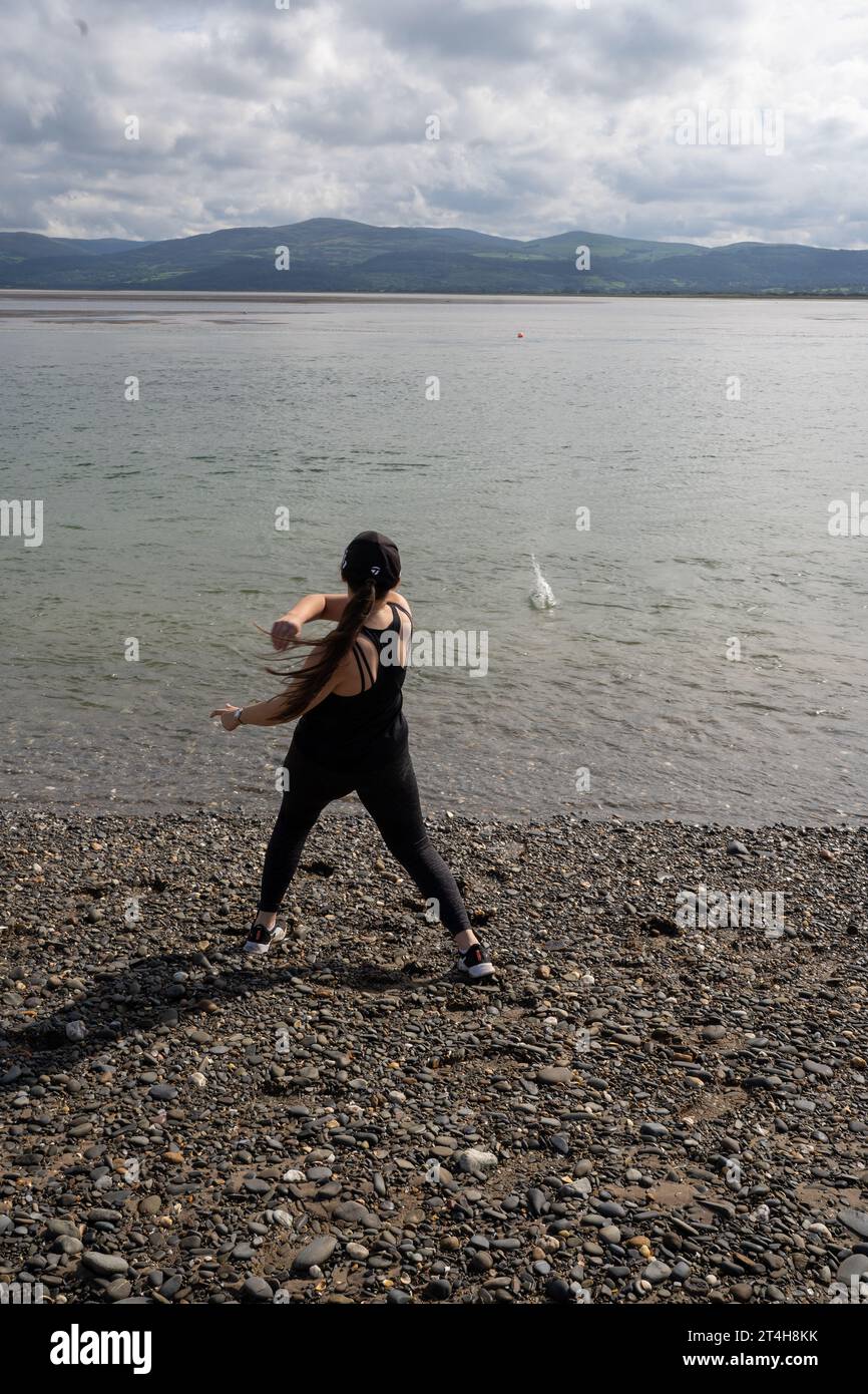 Ein junges Weibchen, das Steine im Meer in Aberaeron Beach überspringt Stockfoto