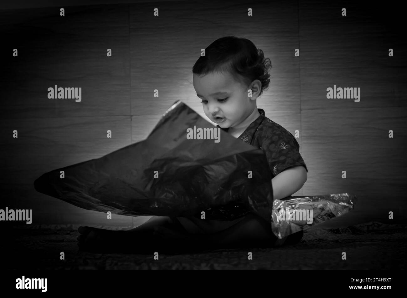 Niedliches Kleinkind Baby Junge, das mit Knitterpapier in Schwarz-weiß spielt Stockfoto