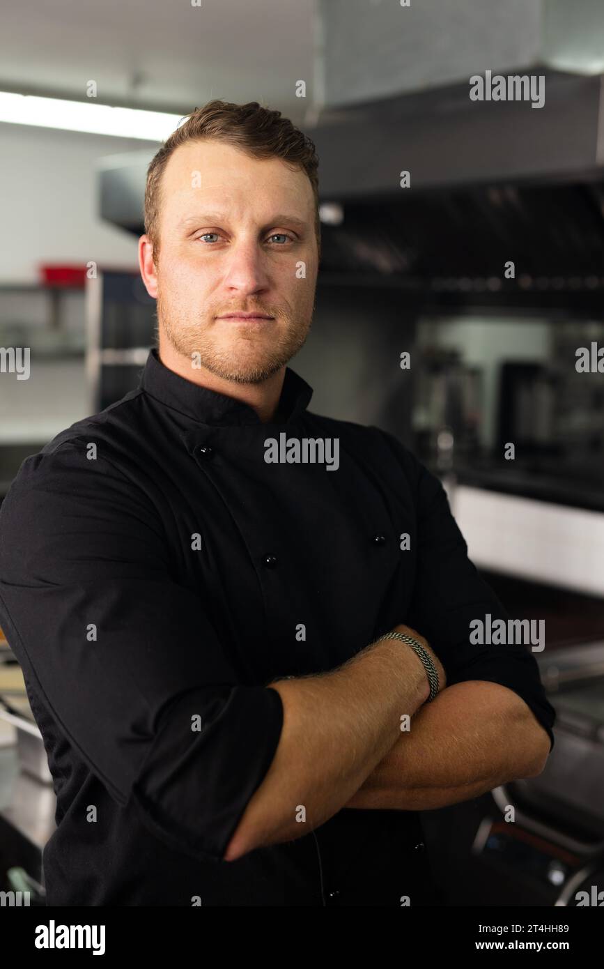 Selbstbewusster männlicher Chefkoch in schwarzer Uniform mit überkreuzten Armen in der Küche Stockfoto