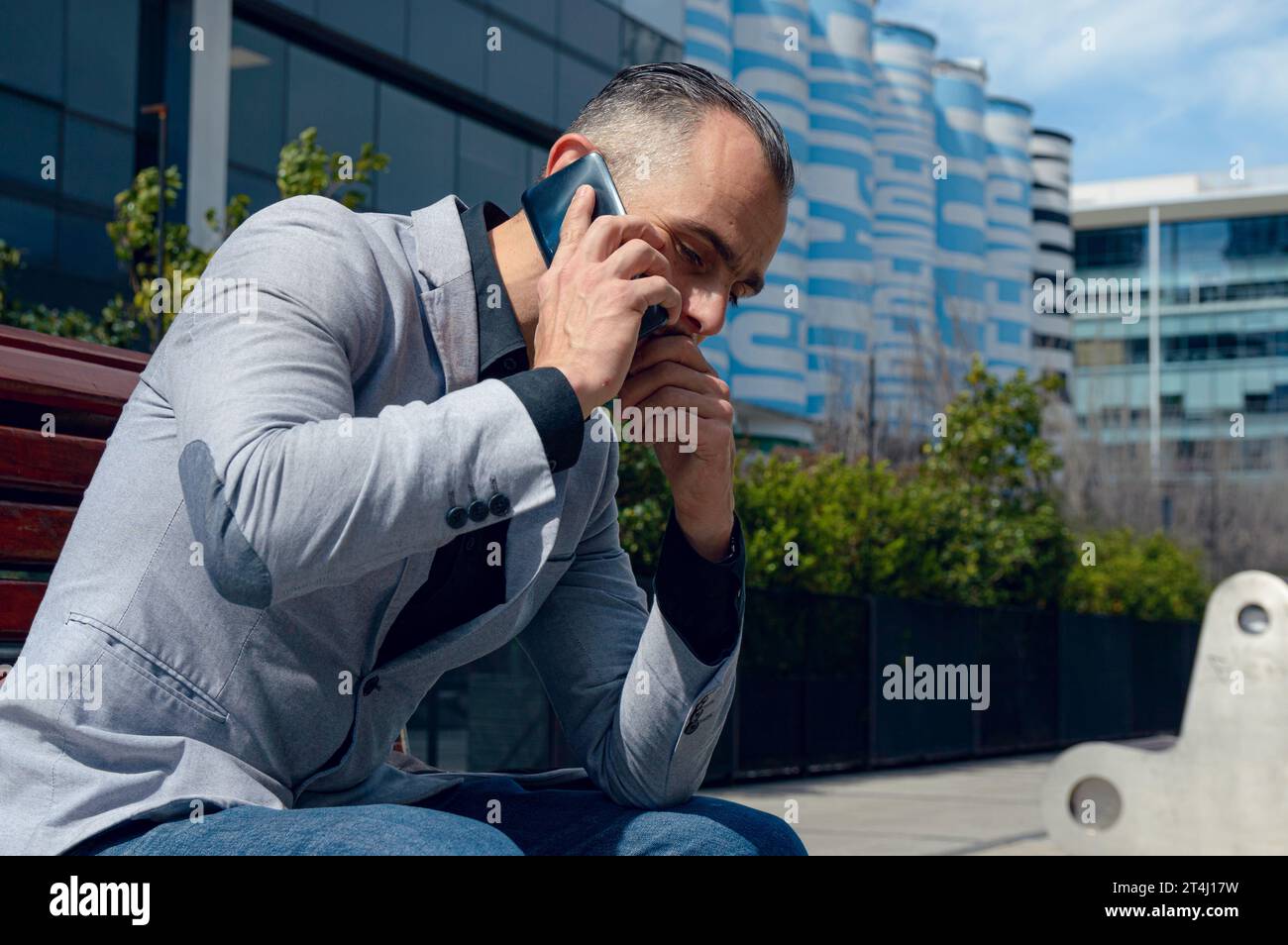 Kaukasischer Erwachsener Geschäftsmann, mit grauer Jacke und kurzen Haaren, sitzt sehr nachdenklich besorgt am Telefon im Freien, Business und Technologie Co Stockfoto