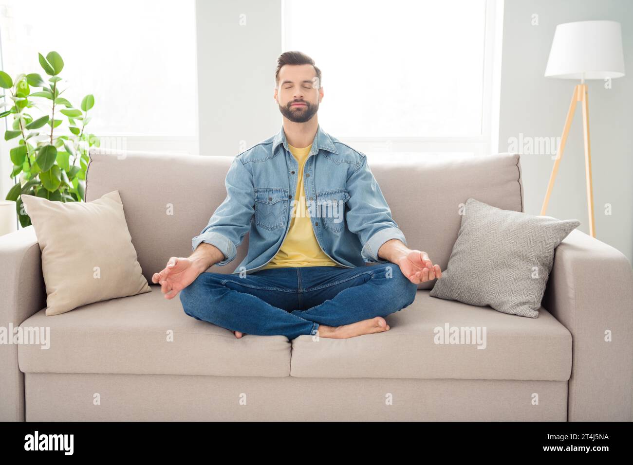 Body-Size-Junge Millennials in Jeans-Outfit, meditiert zu Hause auf der Couch Stockfoto