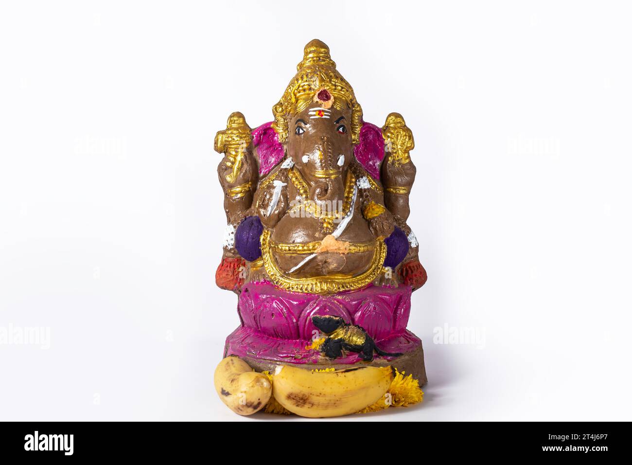 Eine wunderschön gemalte Ganesh-Statue aus Ton auf weißem Hintergrund wird mit Blumen und Bananen gefeiert. Stockfoto