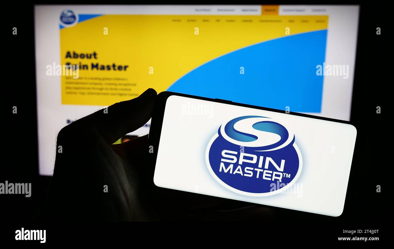 Person mit Smartphone und Logo des kanadischen Spielzeugunternehmens Spin Master Corp. Vor der Website. Schwerpunkt auf dem Display des Telefons. Stockfoto