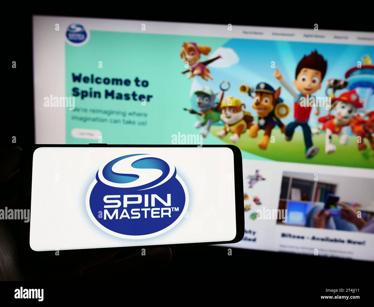 Person, die ein Mobiltelefon mit dem Logo des kanadischen Spielzeugunternehmens Spin Master Corp. Vor der Webseite hält. Schwerpunkt auf dem Display des Telefons. Stockfoto
