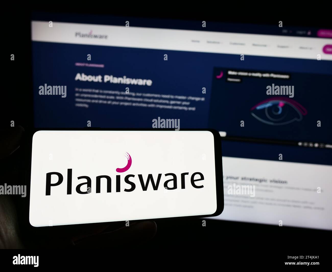 Person, die ein Mobiltelefon mit dem Logo des französischen Softwareunternehmens Planisware SAS vor der Business-Webseite hält. Schwerpunkt auf dem Display des Telefons. Stockfoto