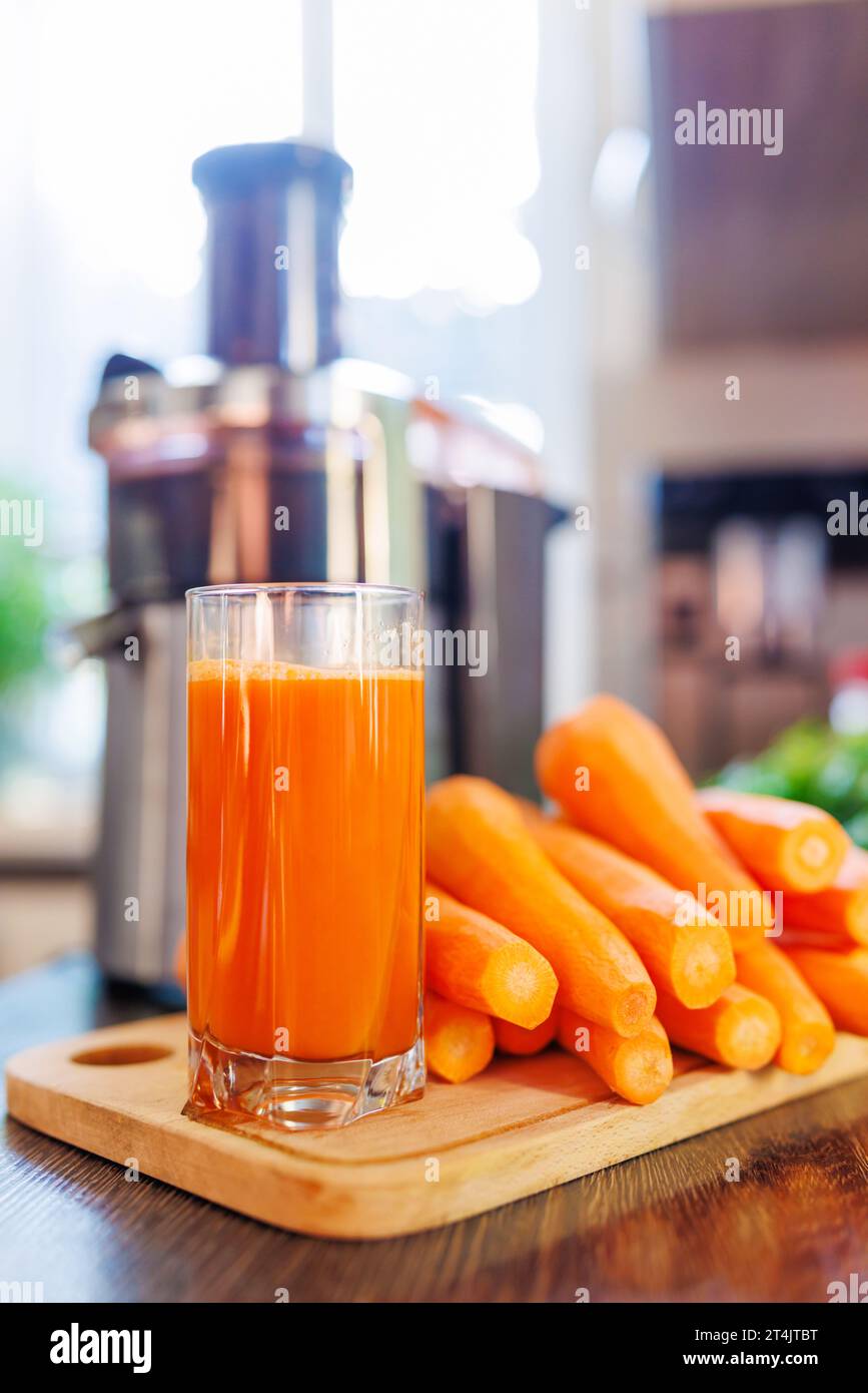 Ein Glas frisch gepressten Karottensaft, Karotten und Saftpresse in der Küche Stockfoto