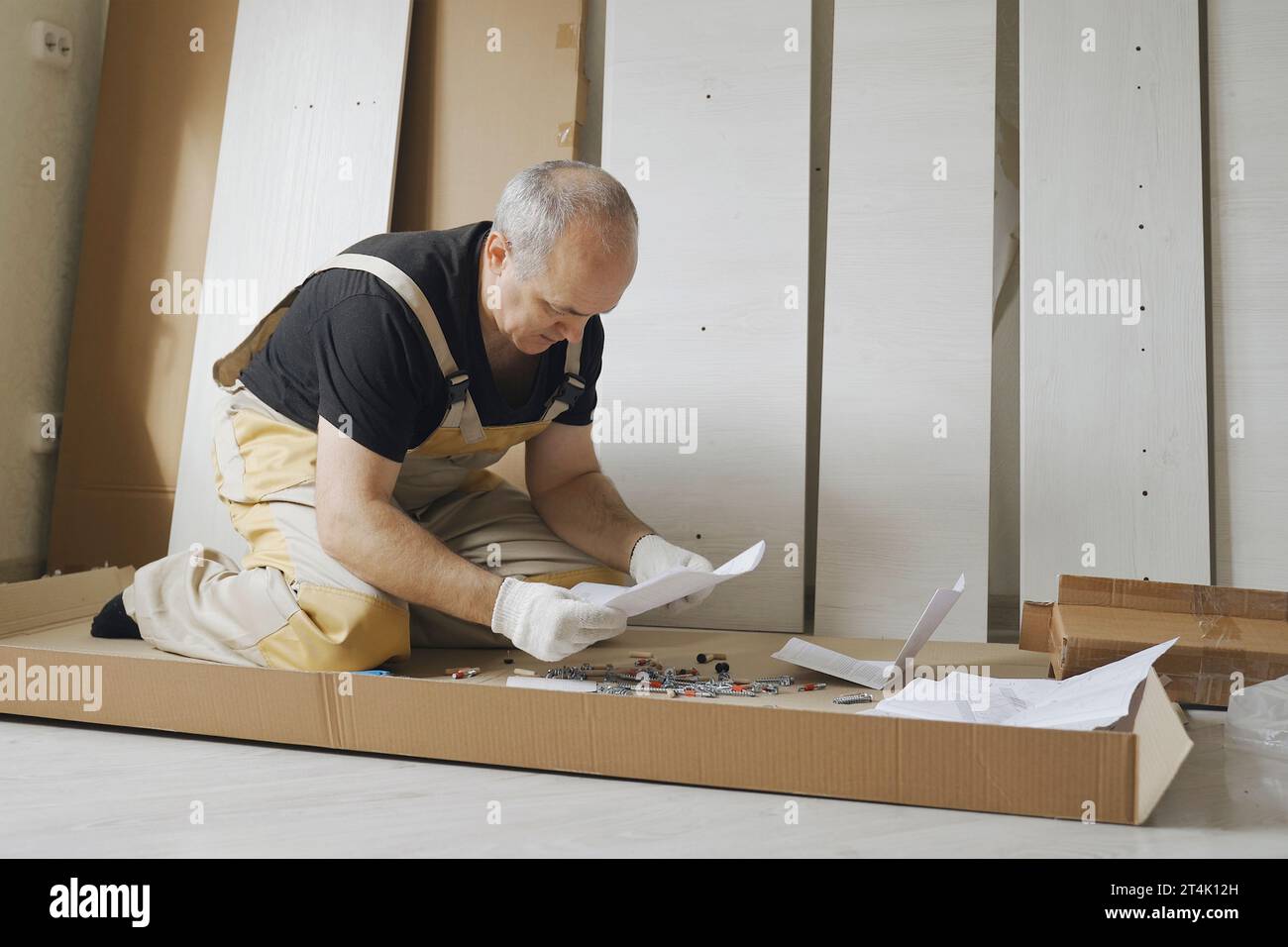 Ein männlicher Arbeiter studiert Anweisungen, bevor er Möbel zusammenbaut. Gesamtplan. Stockfoto