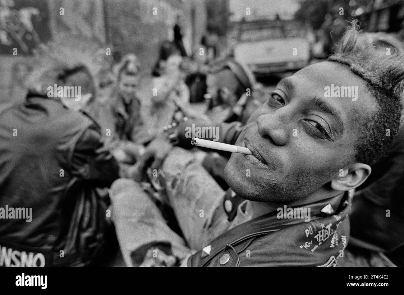 Ein junger schwarzer Punk mit einer Gruppe von Freunden, die auf einem Brixton-Pflaster sitzen. Stockfoto