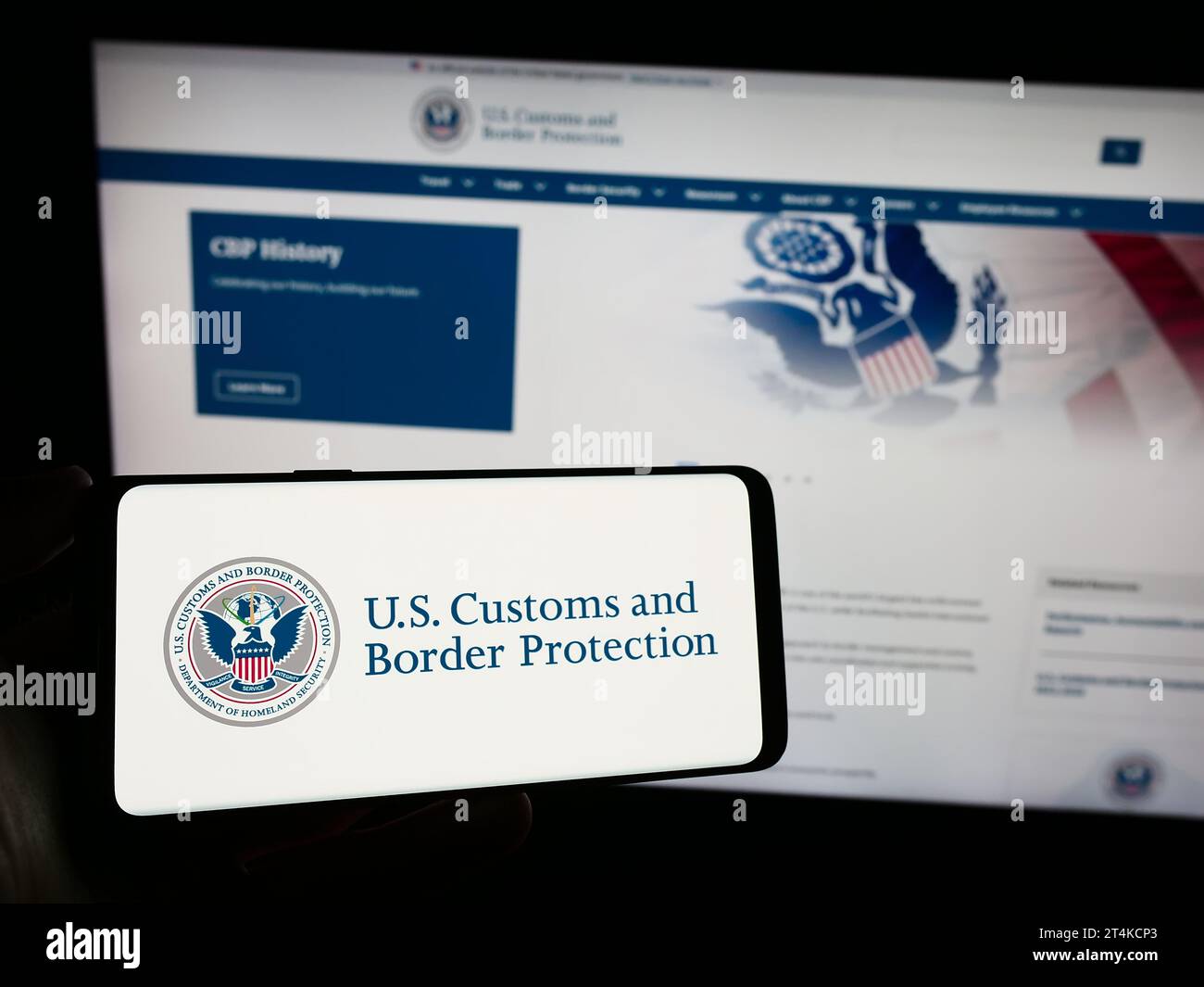 Person, die ein Smartphone mit dem Siegel der Behörde United States Customs and Border Protection (CBP) vor der Website hält. Schwerpunkt auf dem Display des Telefons. Stockfoto