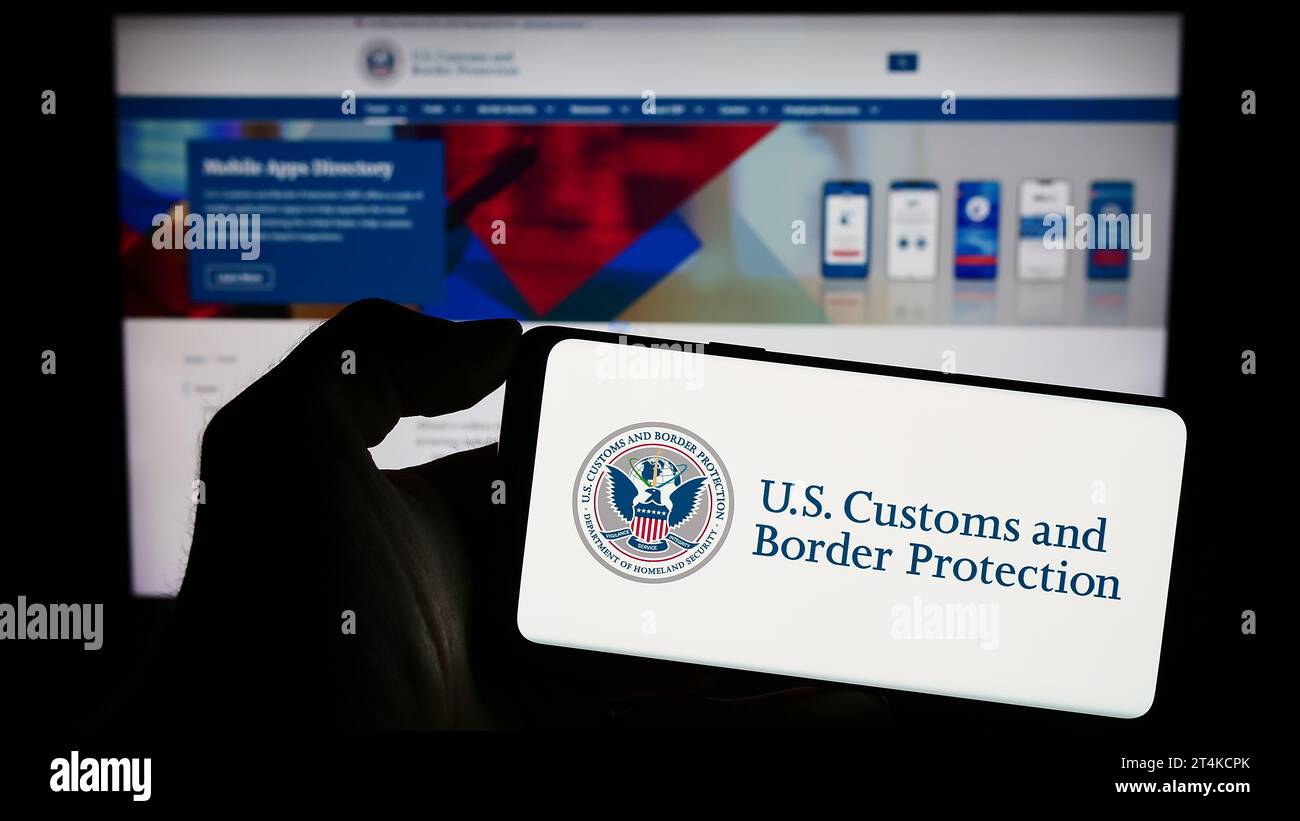 Person, die ein Mobiltelefon mit dem Siegel der Behörde United States Customs and Border Protection (CBP) vor der Webseite hält. Schwerpunkt auf dem Display des Telefons. Stockfoto