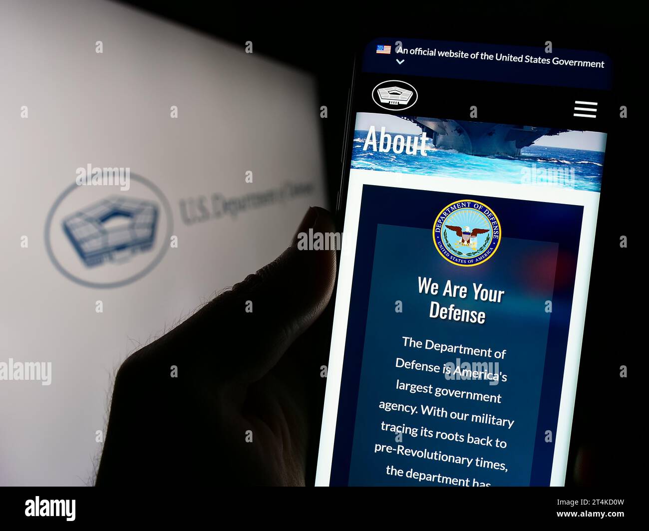 Person mit Smartphone und Webseite des US-Verteidigungsministeriums (DoD) vor dem Logo. Konzentrieren Sie sich auf die Mitte des Telefondisplays. Stockfoto
