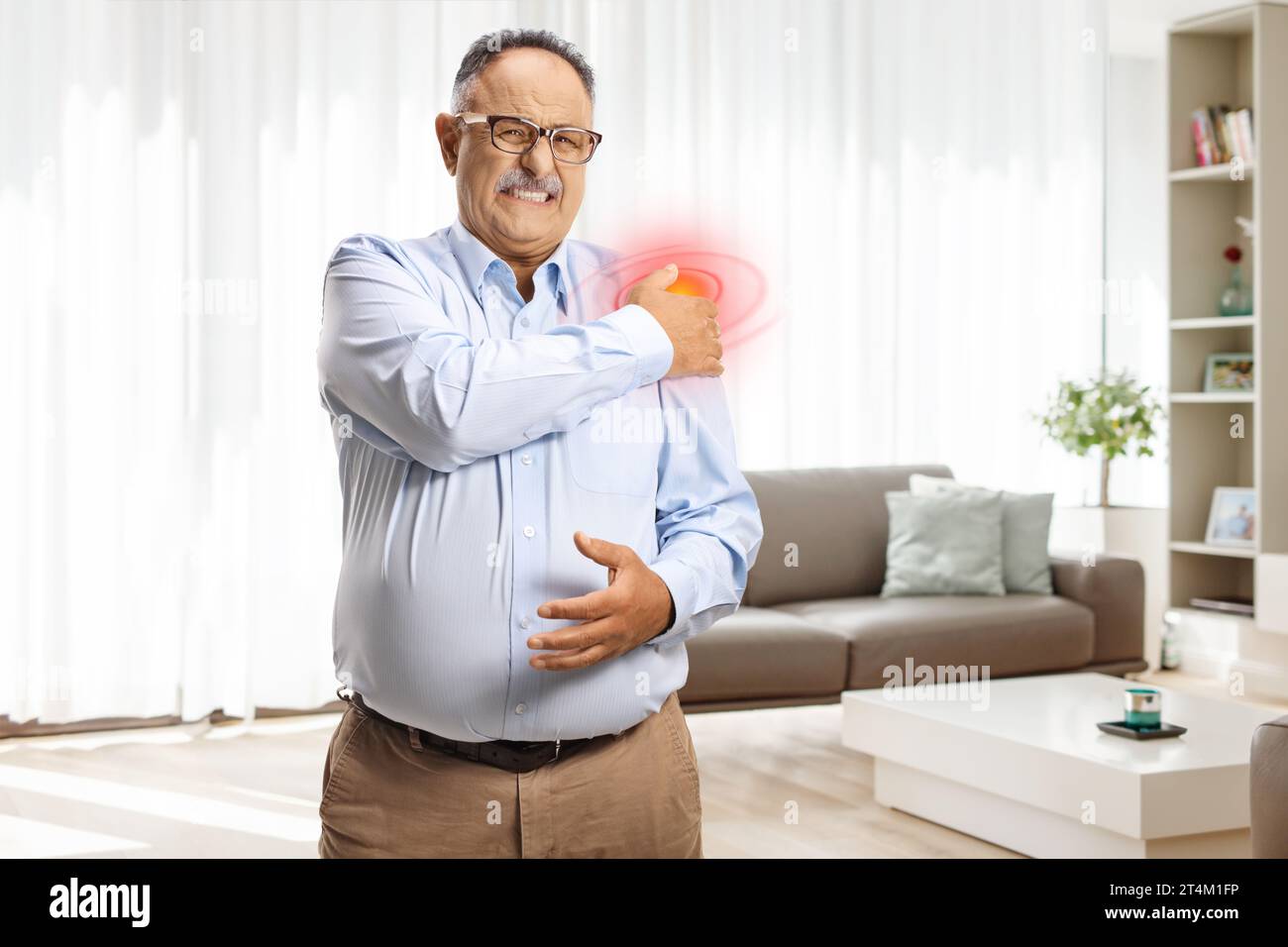 Reifer Mann, der zu Hause steht und Schulter mit rotem Fleck hält, Gesundheitsprobleme Stockfoto