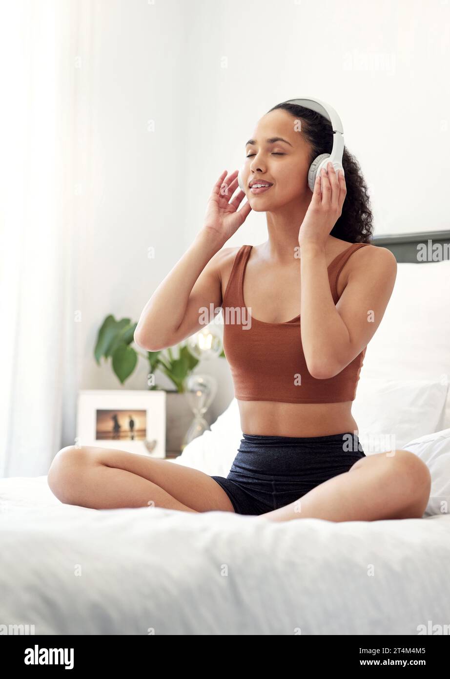 Einatmen von Güte, Ausatmen von Negativität. Eine junge Frau, die Musik hört, während sie zu Hause auf ihrem Bett sitzt. Stockfoto