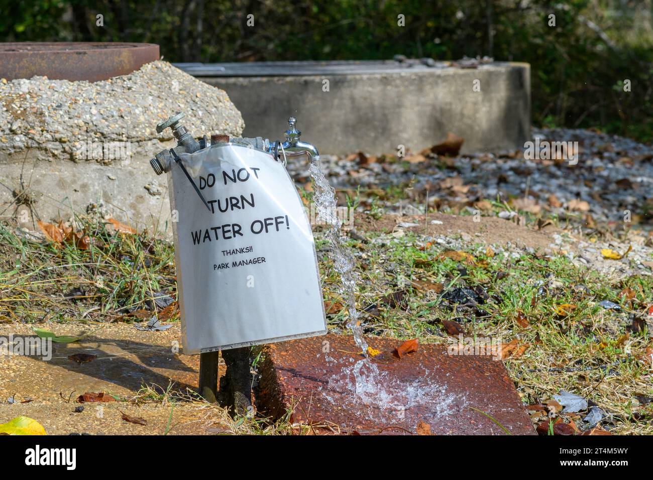 Ein neuer Wasserhahn lässt Wasser neben einem alten Wasserhahn laufen, der ausgeschaltet ist und auf dem Schild steht, dass „Don't Turn Water Off“ (Wasser nicht ausschalten) im Lake Fausse Pointe State Park, LA, USA Stockfoto