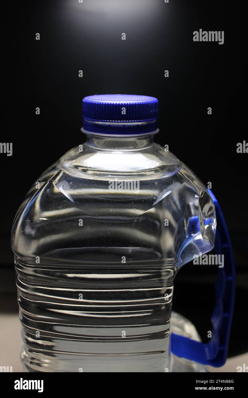 Eine große Flasche mit einem Kunststoffgriff, gefüllt mit sauberem Wasser auf schwarzem Hintergrund Stockfoto