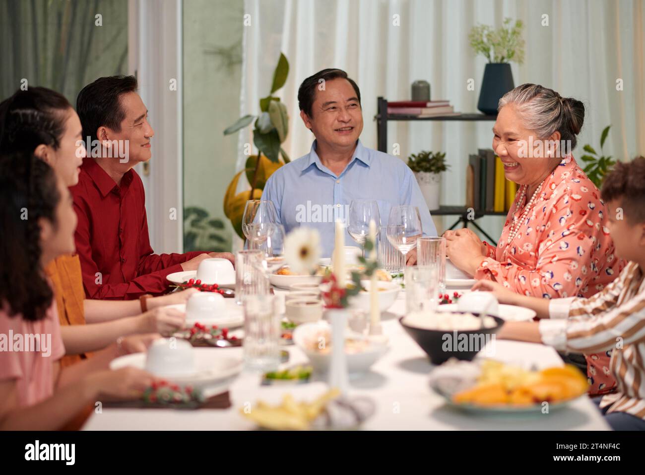 Glückliche vietnamesische Familie unterhielt sich am großen Esstisch, wenn sie versammelt war, um Feiertage zu feiern Stockfoto