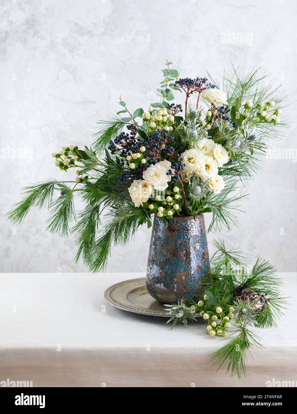 Wunderschöner Winterstrauß in Vase. Blumenarrangements mit Rosen, Tannenzweigen, Winterbeeren, Eukalyptus und eryngium. Weihnachtsblumendekoration. Stockfoto