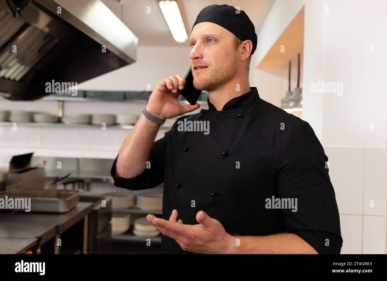Kaukasischer Küchenchef spricht über Smartphone und gestikuliert in der Restaurantküche, Kopierraum Stockfoto