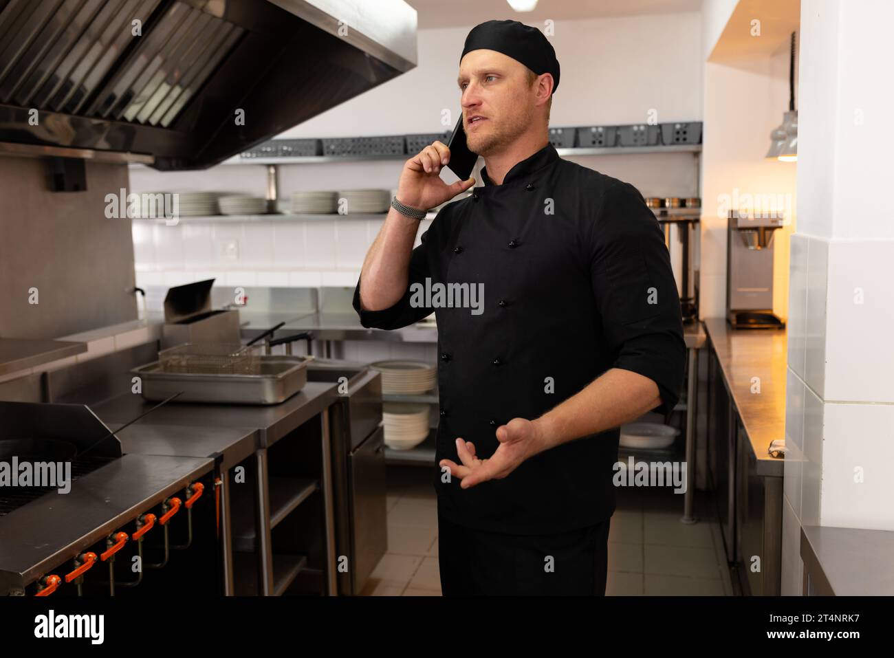 Konzentrierter kaukasischer Küchenchef, der auf dem Smartphone spricht und in der Restaurantküche gestikuliert Stockfoto