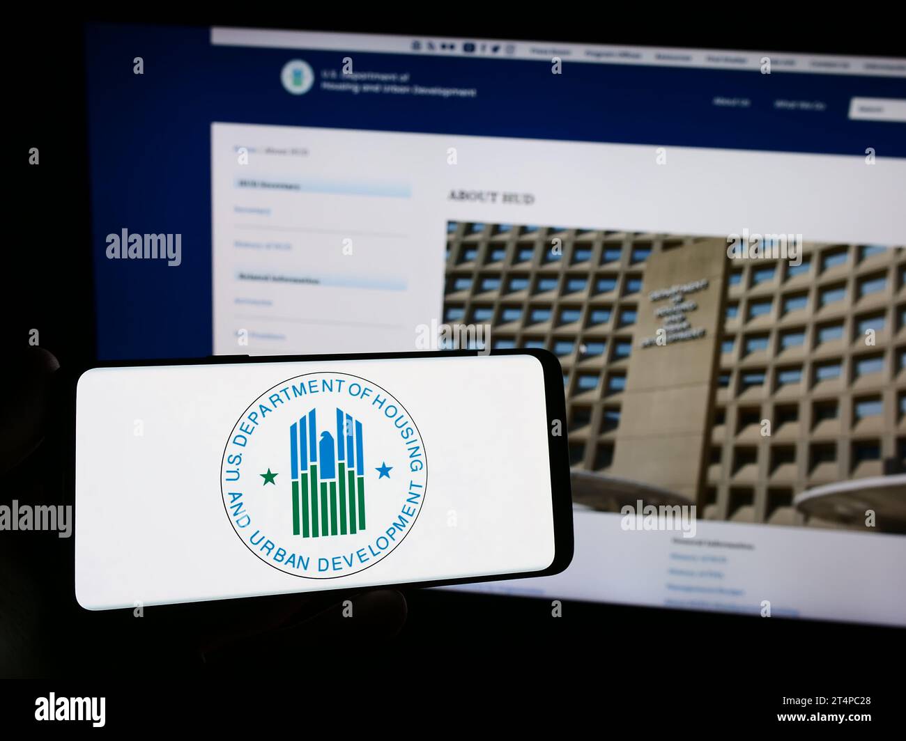 Person mit Smartphone und Logo des US Department of Housing and Urban Development (HUD) vor der Website. Schwerpunkt auf dem Display des Telefons. Stockfoto