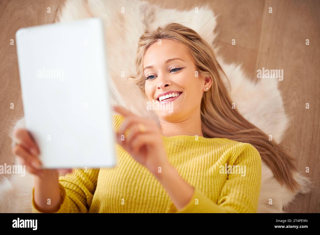Über tausend Freundschaftsanfragen. Eine junge Frau, die auf dem Boden liegt und ihr digitales Tablet hält. Stockfoto