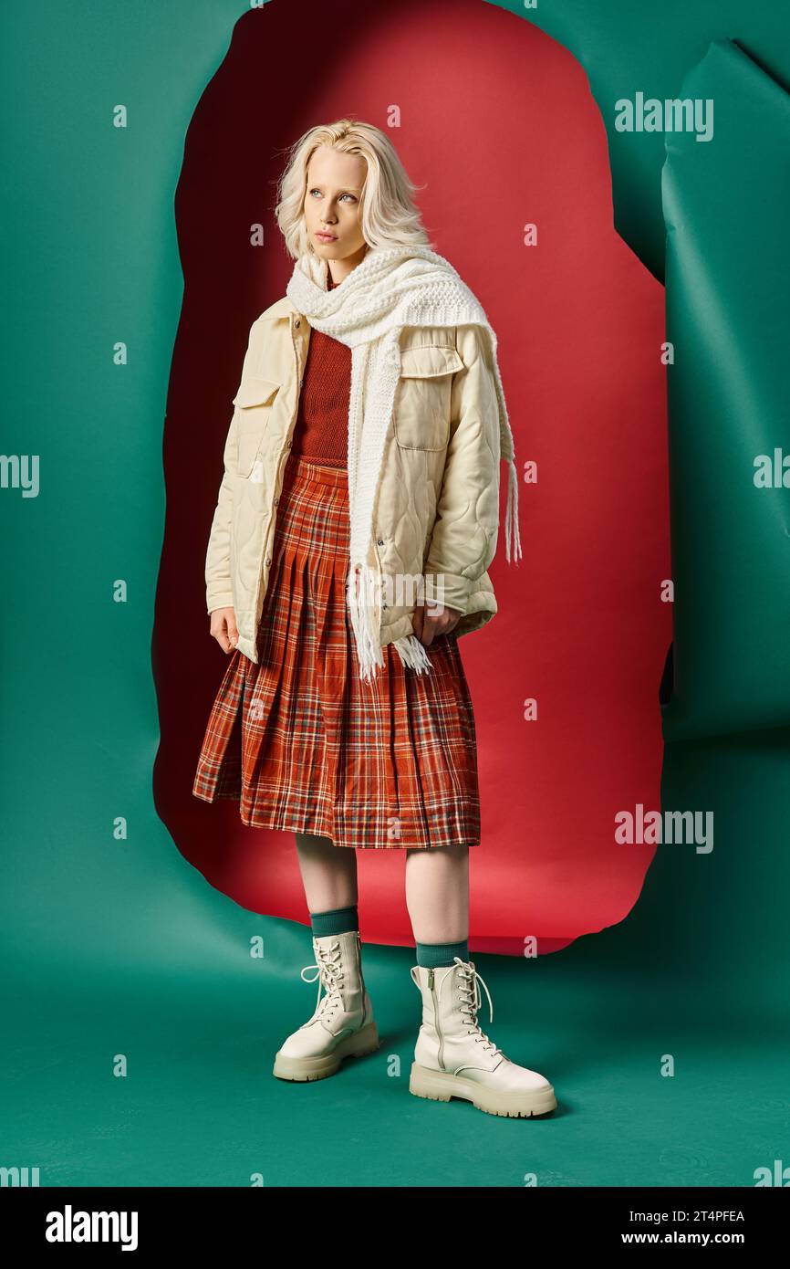 Die ganze Länge einer jungen blonden Frau im Winteroutfit posiert auf rot mit türkisfarbenem Hintergrund Stockfoto