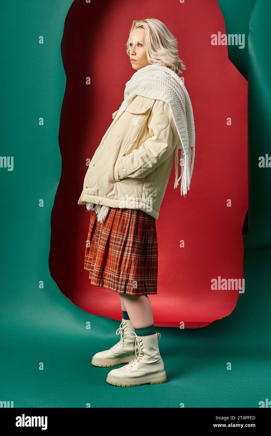 Die ganze Länge der blonden Frau in stilvollem Winteroutfit posiert auf rot mit türkisfarbenem Hintergrund Stockfoto