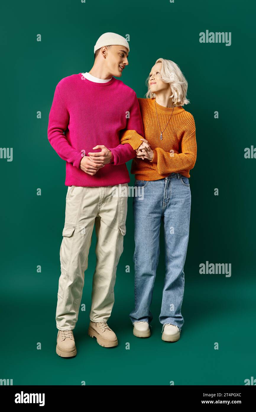 Glückliches Paar in Winterpullover, die Hand an Hand auf türkisfarbenem Hintergrund stehen, junge Frau und Mann Stockfoto