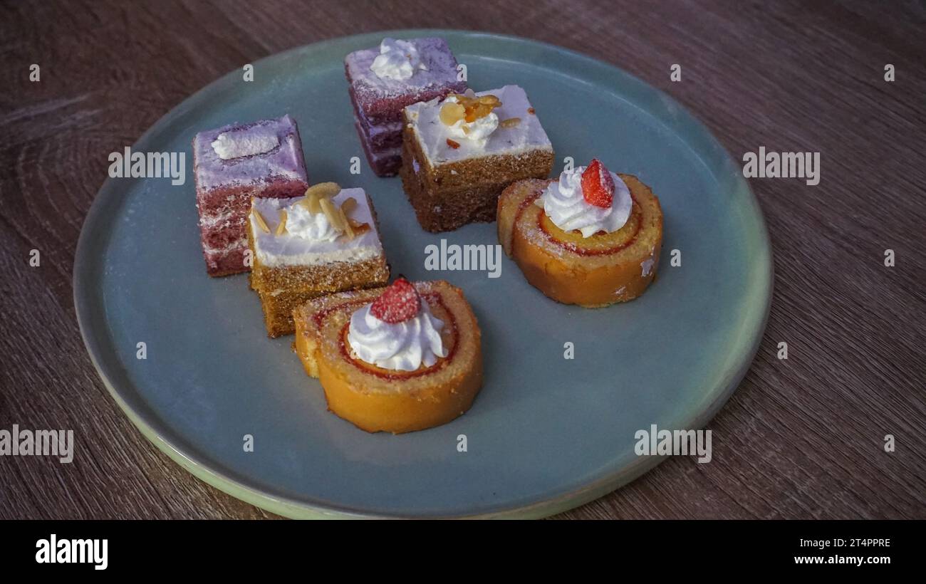 Kleine Kuchen mit schönen und frischen Belägen, Schichtkuchen und gerollte Kuchen werden am Tisch serviert Stockfoto