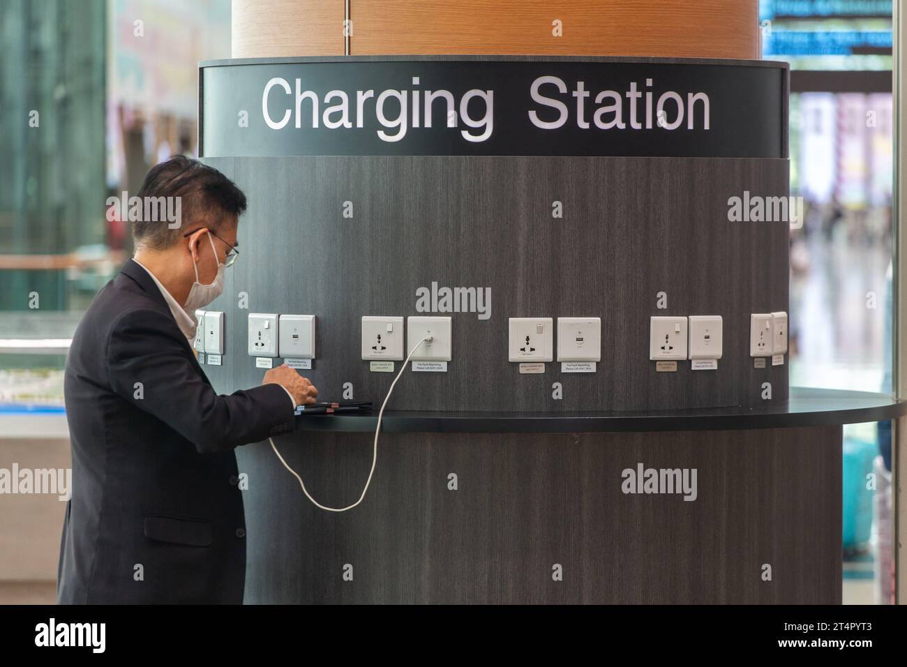 Männlicher Reisender, der seinen kostenlosen Service zum Aufladen seines Telefons nutzt, um in Verbindung zu bleiben, Ladestation im Abflugbereich von Terminal 3. Flughafen Changi. Singapur. Stockfoto