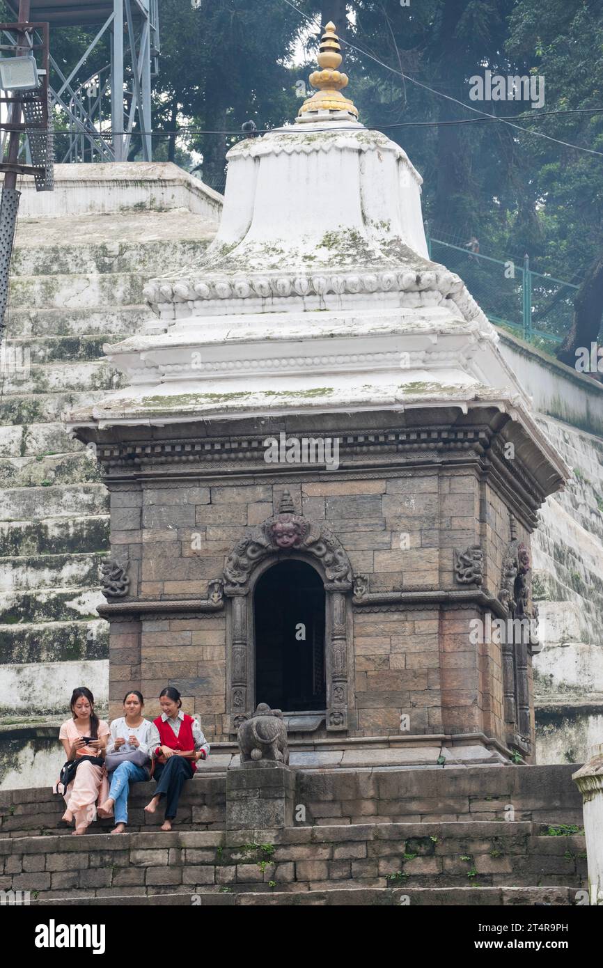 Kathmandu, Nepal: hindu-Mädchen auf der Treppe eines Minitempels am Ufer des heiligen Bagmati-Flusses, Einäscherungszeremonie im Pashupatinath-Tempel Stockfoto