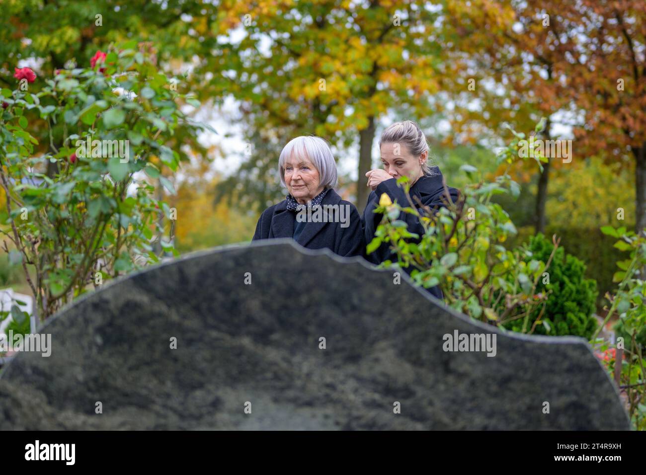 Nahaufnahme von Mutter und Tochter, die am Grab des Mannes auf dem Friedhof stehen, die Mutter blickt in die Ferne, die Tochter wischt sich die Nase, auf A Stockfoto