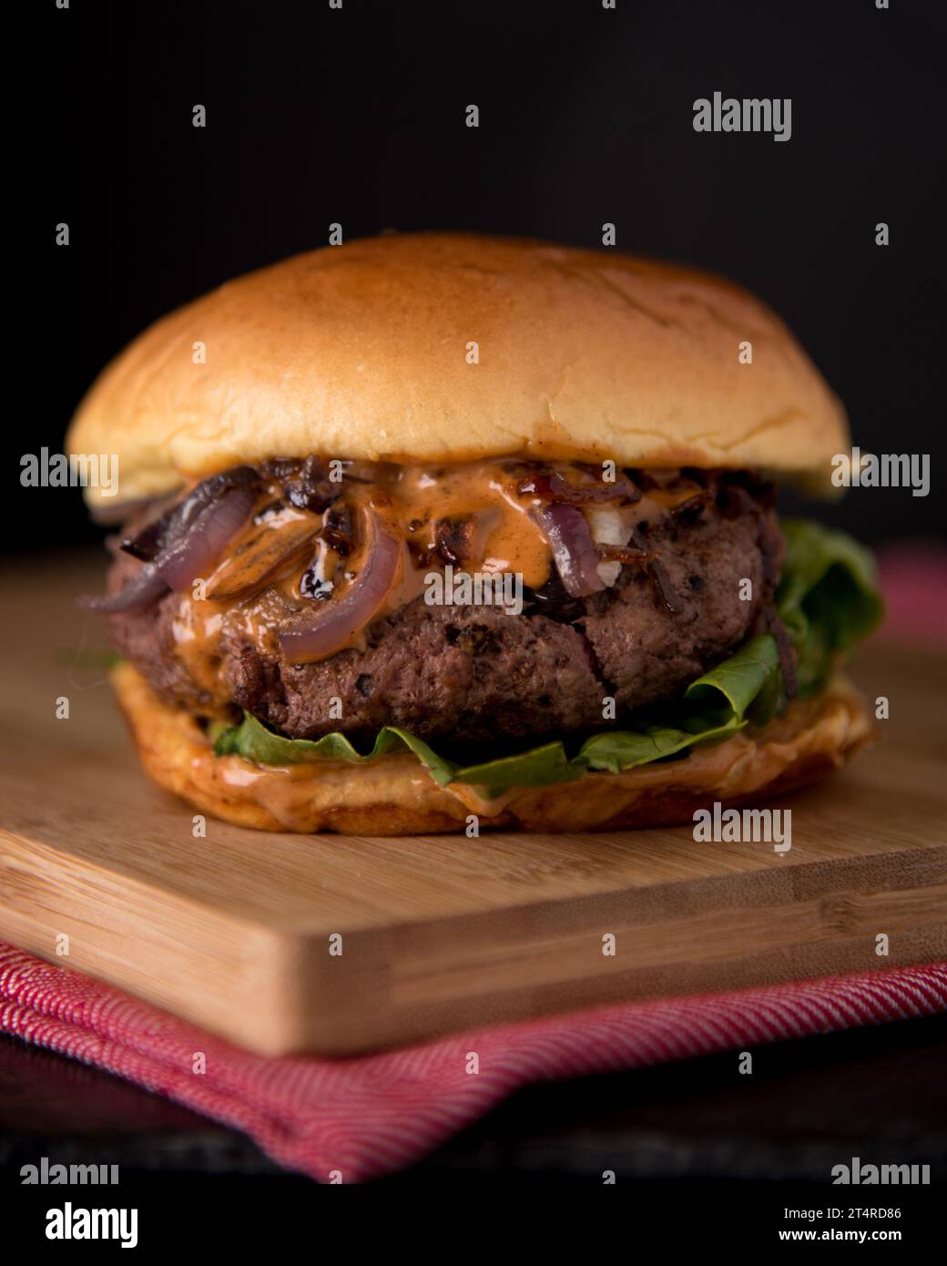 Saftiger hausgemachter Burger mit Salatzwiebeln und chipotle-Sauce in einem Brioche-Brötchen. Dunkler und stimmungsvoller Hintergrund. Stockfoto