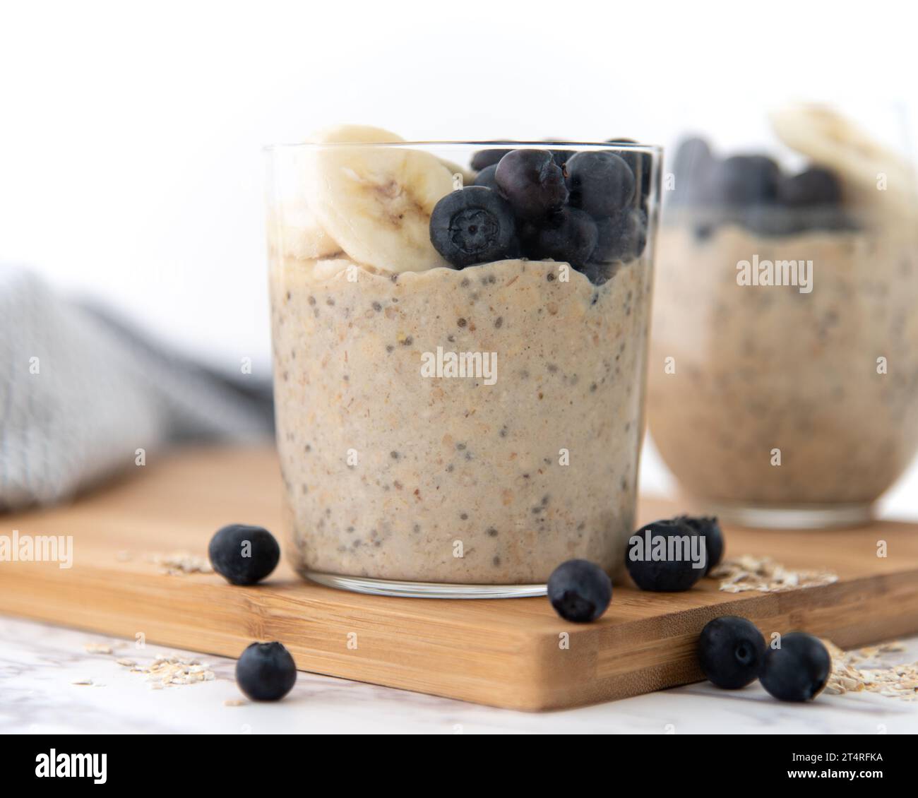 Ein gesundes Frühstück mit über Nacht Hafer auf einem hölzernen Schneidebrett und weißem Hintergrund. Garniert mit Banane und Heidelbeeren Stockfoto