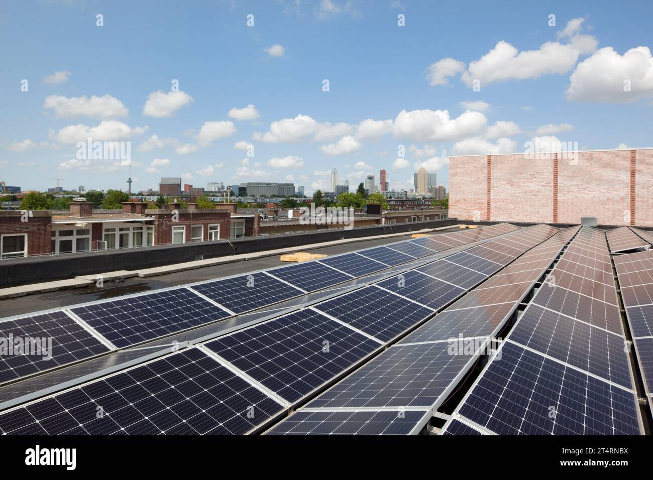 Solarpaneele auf dem Dach vor klarem Himmel, mit Rotterdamer Skyline. Theater Zuidplein, Rotterdam, Rotterdam, Niederlande. Architekt: De Zwarte Hond, 2020. Stockfoto