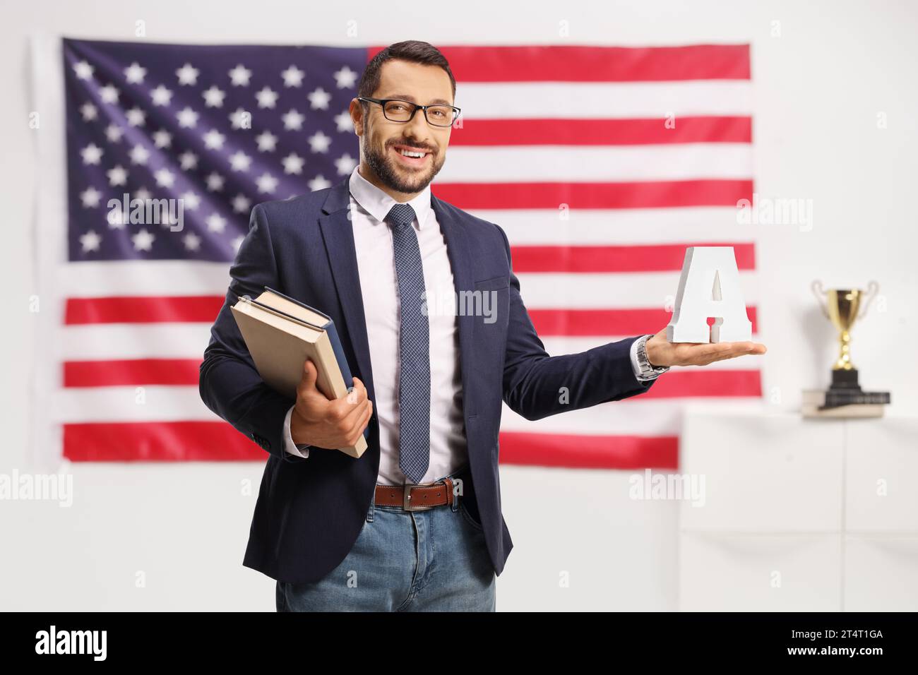Junger Mann mit Brille, der Bücher hält und den Buchstaben A vor einer US-Flagge Stockfoto